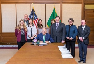 Staff from various government entities and non-profits smiling as Governor Jay Inslee signs a product stewardship bill. 