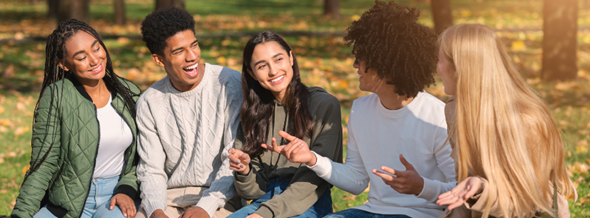 group of young multicultural kids sitting on the grass smiling and talking