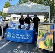 Three people tabling with I secure my load for safer roads pledge board.