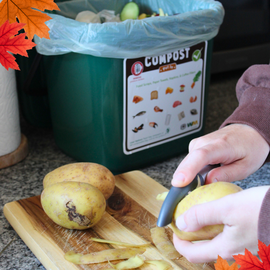Person peeling potatoes with a compost kitchen caddy in the background filled with food waste and scraps.