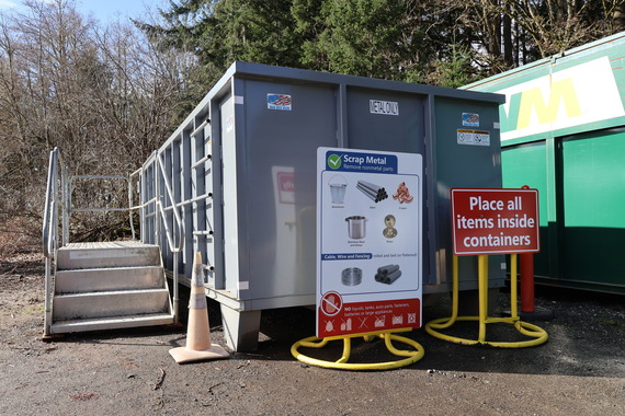 Scrap metal container with stairs on the side of it. Sign in front guiding residents to place all items inside container.