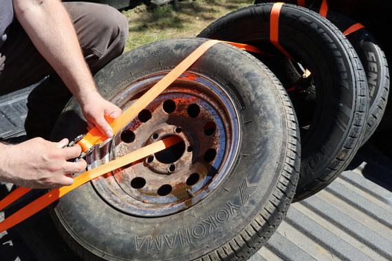Tires in the back of a truck with a ratchet strap threaded through and over the tires.