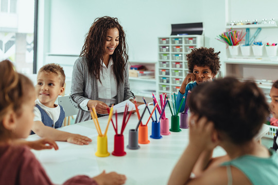 female teacher around table with five children