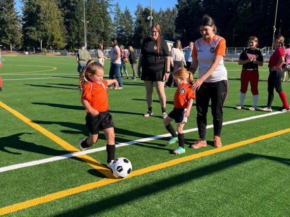 A girl in an orange jersey kicks soccer ball
