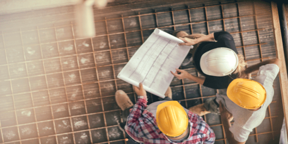 aerial view of construction workers wearing hard hats looking at a blueprint on a job site