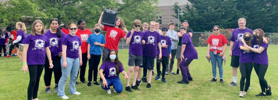 Students from Edgemont Junior High wearing red and purple shirts stand in grassy field.