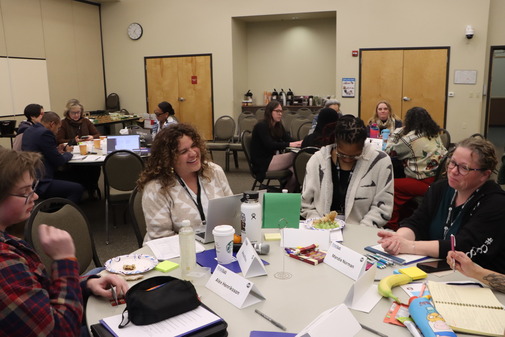 A group of task force members sit around a table discussing their hopes for graduation requirements. Three similar tables are in the background.
