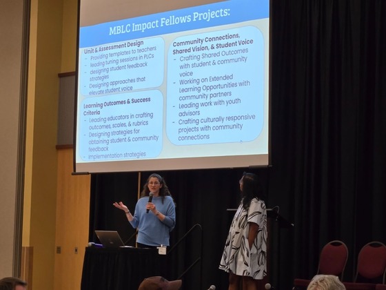 Two people on a stage presenting in front of a projector