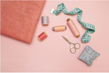 Cloth, thread, scissors, pin cushion with pins, and measuring tape