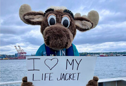 Mariner Moose holding a sign that says "I Love My Lifejacket"