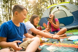 Three children play on a blanket in front of a tent.