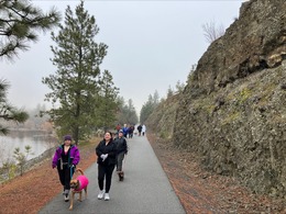 Walkers with dog on paved path with river on one side and basalt cliffs on the other.