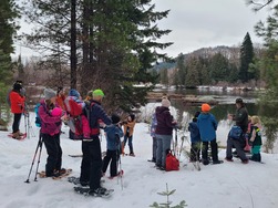 A group of snowshoers listen to a ranger who stands in front of a lake, talking.