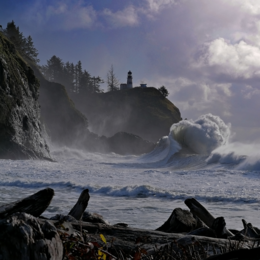 Big waves crash under a lighthouse at Cape Disappointment with beach wood in the foreground