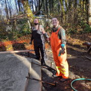 Two park aides, one in an orange jumpsuit, stand on a trail, digging in the dirt.