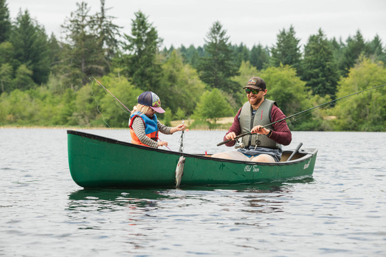 Man and child out fishing on a canoe on a calm lake while wearing life jackets