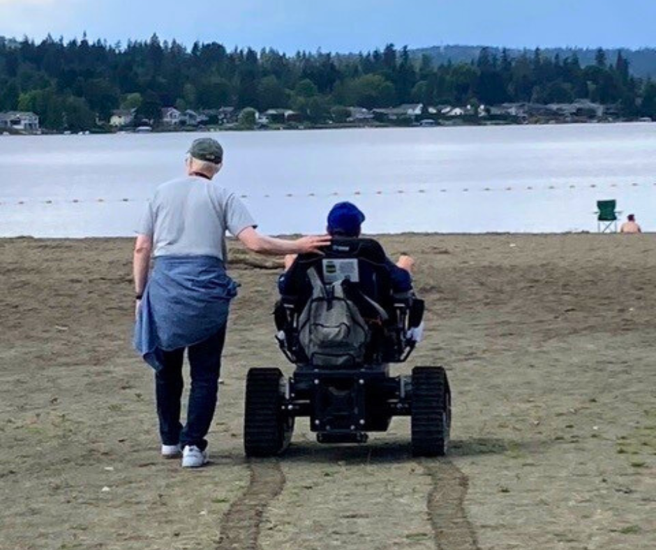 one person using the new track chair at Lake Sammamish and another person walking alongside them at the beach