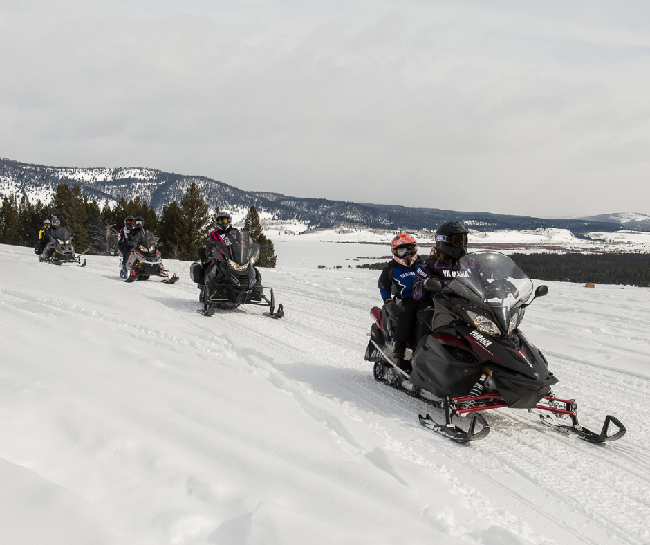 four double snowmobiles riding around on a snowmobile trail at a Sno-Park on a cloudy day