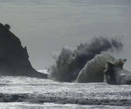 Giant waves crashing at the coast of Cape Disappointment with the lighthouse on top of a rock in the background