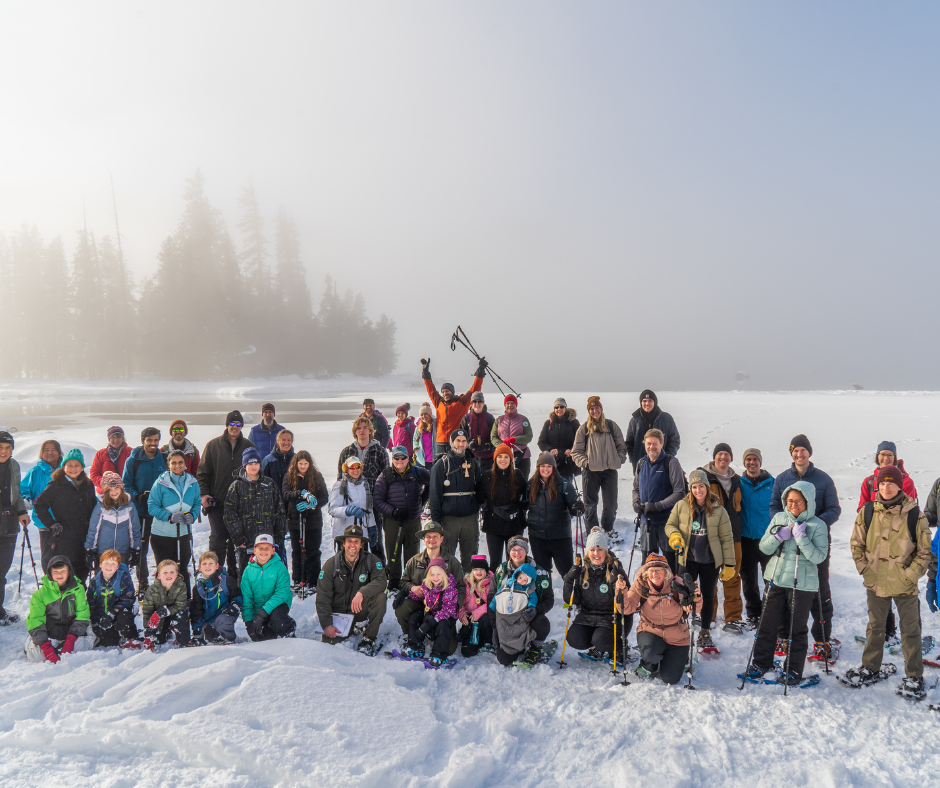 Large group photo of people participating in Lake Wenatchee's First Day Hikes snowshoe event in winter gear and snowshoes in front of the lake