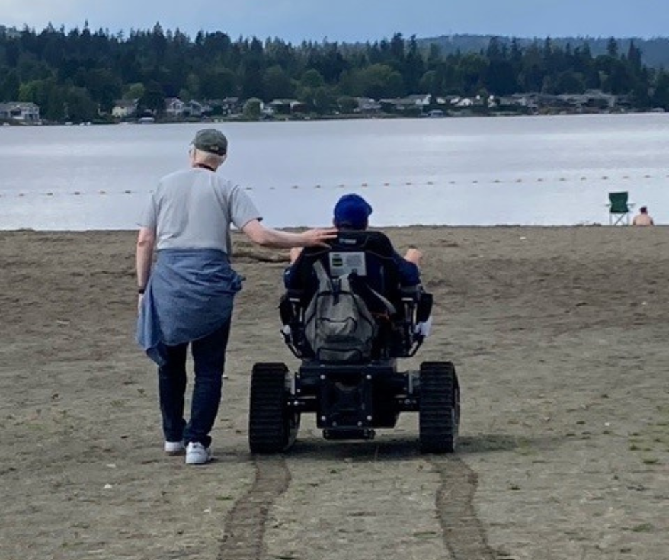 One person using the new track chair at Lake Sammamish and another person walking alongside them at the beach