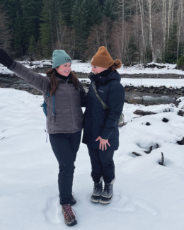 Two women at Easton Reload Sno-Park's First Day Hikes event posing in front of Cabin Creek smiling and having fun in the snow