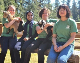 Four students sitting next to goats at a farm