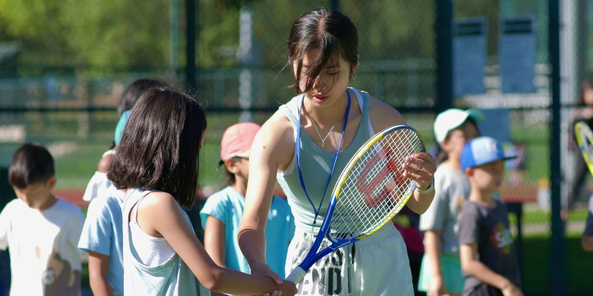 Teenage day camp leader helping a young child learn to hold a tennis racket