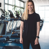 Fitness attendant smiling while standing near a row of elliptical machines