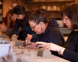 Three adults hand-building butter dishes out of clay in the Old Redmond Schoolhouse studio
