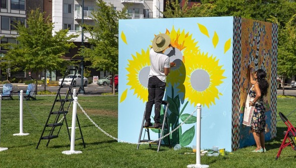 Muralists painting a 8 foot by 8 foot freestanding mural of sunflowers in Downtown Park