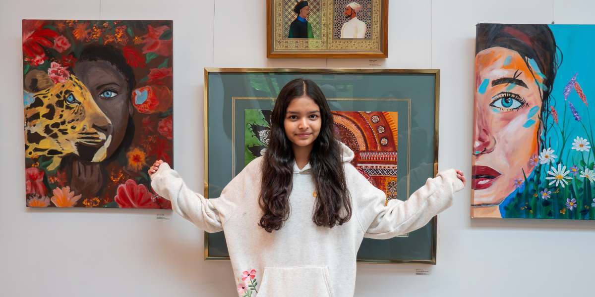 Young artist standing in front of their artwork on display