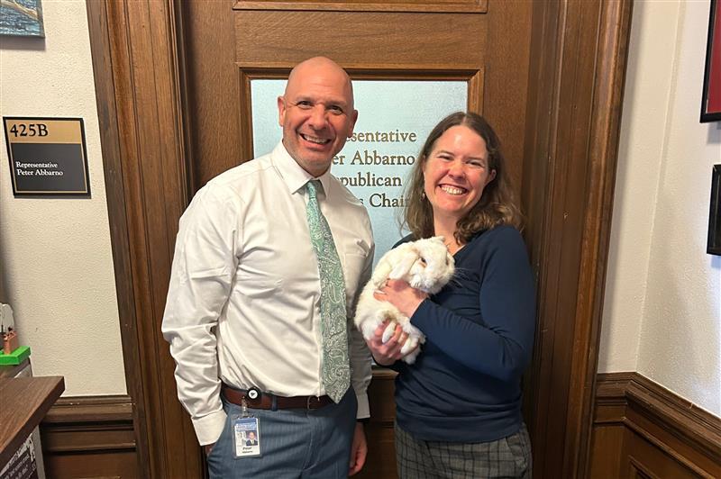 A man and a women smiling for the camera. The women is holding a white bunny rabbit.