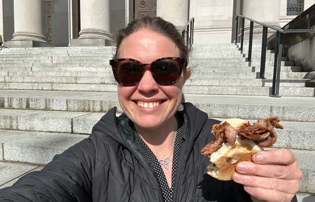 A women in sunglasses holds a beef sandwich. 