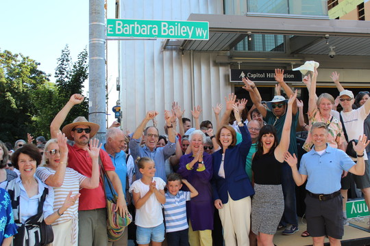 Photo of a crowd smiling and cheering underneath the newly-installed Barbara Bailey Street Sign