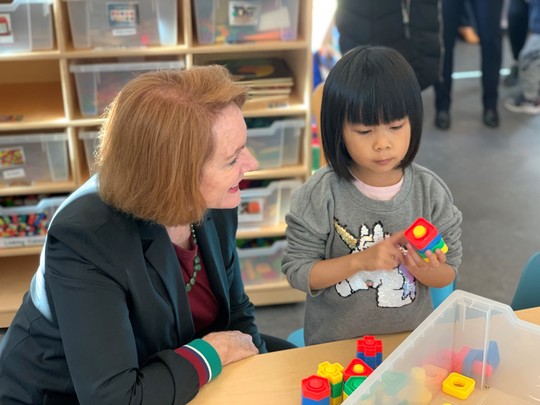 Mayor Durkan crouches next to a preschooler playing with blocks and smiles.