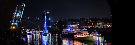 Boats lined with holiday lights float through Seattle's Montlake Cut at night