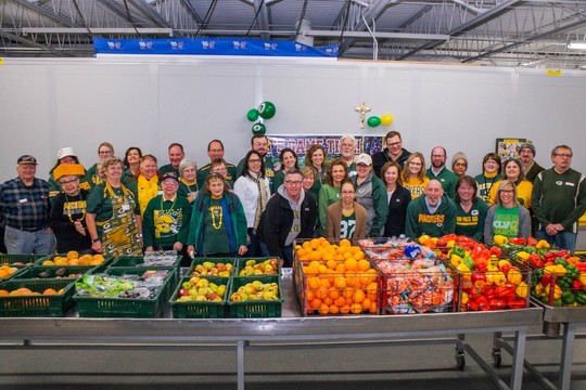 Volunteers from the City of Green Bay pose for a group photo behind baskets of fresh vegetables wearing green and gold 