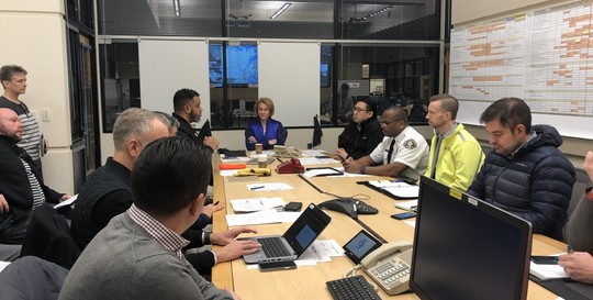 Mayor Durkan sits at the head of a table in the Emergency Operations Center, surrounded by her Cabinet and emergency executives