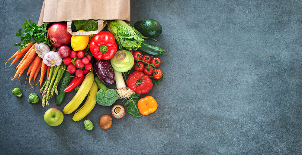 Image of fresh fruits and vegetables pouring out of a paper grocery bag