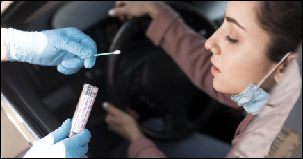Photo of a young woman who is receiving a COVID-19 test conducted through a nasal swab at a drive-in testing center.