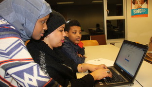 Three youth gathered around a laptop computer