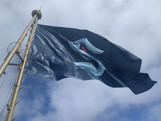 Dark Blue flag flying against a cloudy blue sky at the Space Needle with the Seattle Kraken logo 