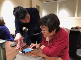 Technology Matching Fund recipient Kin On, a young man helping an elder with navigating her cell phone.