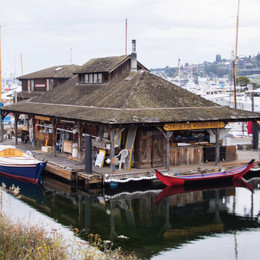 A floating, wooden building on the edge of a lake with small boats tied up on the dock