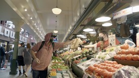 An individuals wearing a face mask purchases produce from an outdoor food market