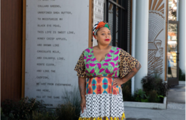 An artist dressed in a multipattern dress and headwrap stands in front of her work at the Jackson Apartments complex in the Central District.. 