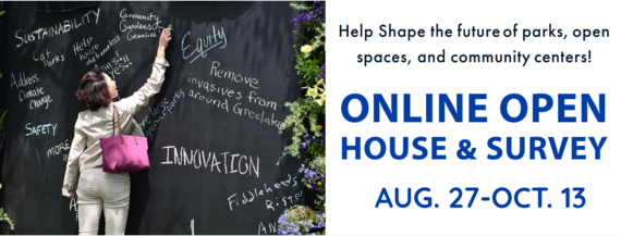 A woman is writing down park suggestions on a large  blackboard outdoors in a park.