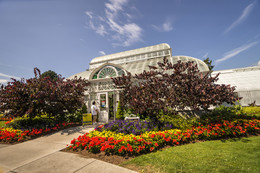 A large white building (the Volunteer Park Conservatory) surrounded by flowers on a sunny day