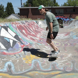 A skateboarder rides through a half pipe covered in graffiti tags